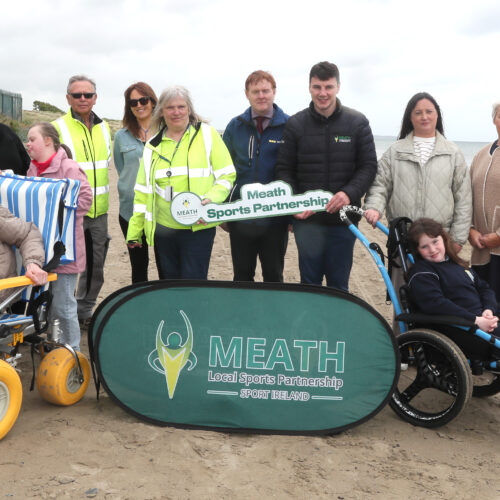 Group of people standing on a beach with two people in beach wheelchairs