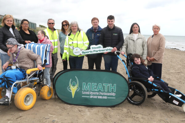Group of people standing on a beach with two people in beach wheelchairs