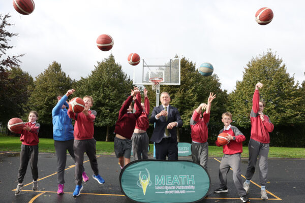 Minister Thomas Byrne T.D. with a group of schoolchildren throwing basketballs up in the air on the new 3x3 Basketball Court in Dunshaughlin.